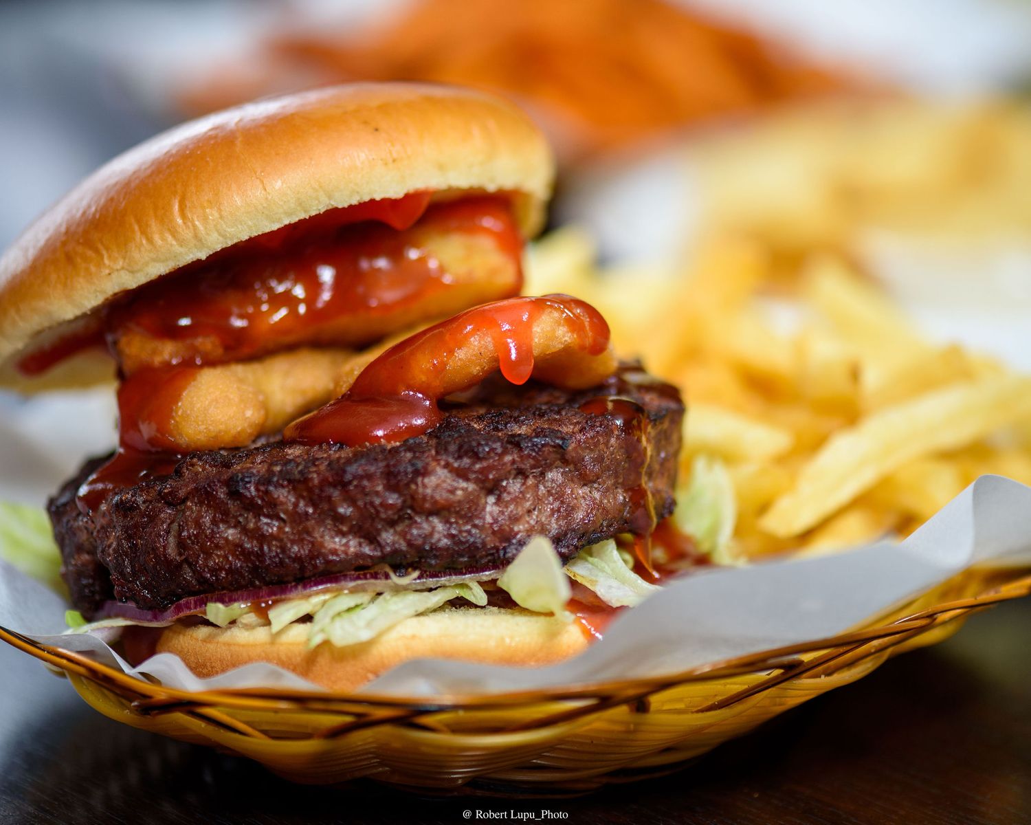 Juicy beef burger with ketchup and onion rings served in a basket with golden french fries.