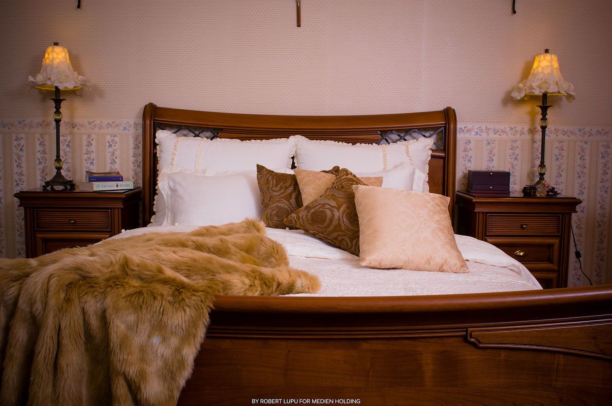 Elegant bedroom with sleigh bed, white linens, fur throw, decorative pillows, and warm bedside lamps.