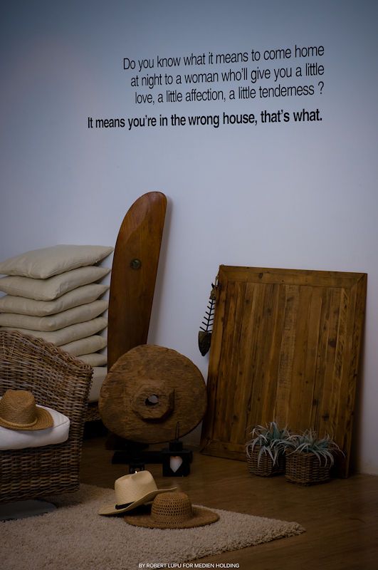 Rustic home decor display with wicker chair, wooden boards, straw hats, and inspirational quote on white wall.