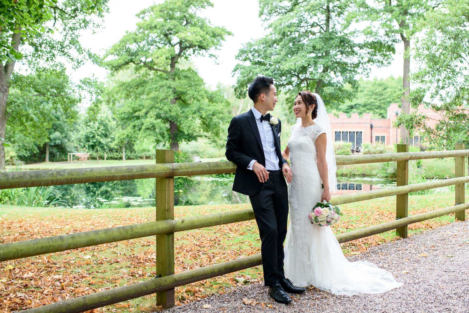 Bride and groom standing by a wooden fence in a lush garden, sharing a romantic moment on their wedding day.