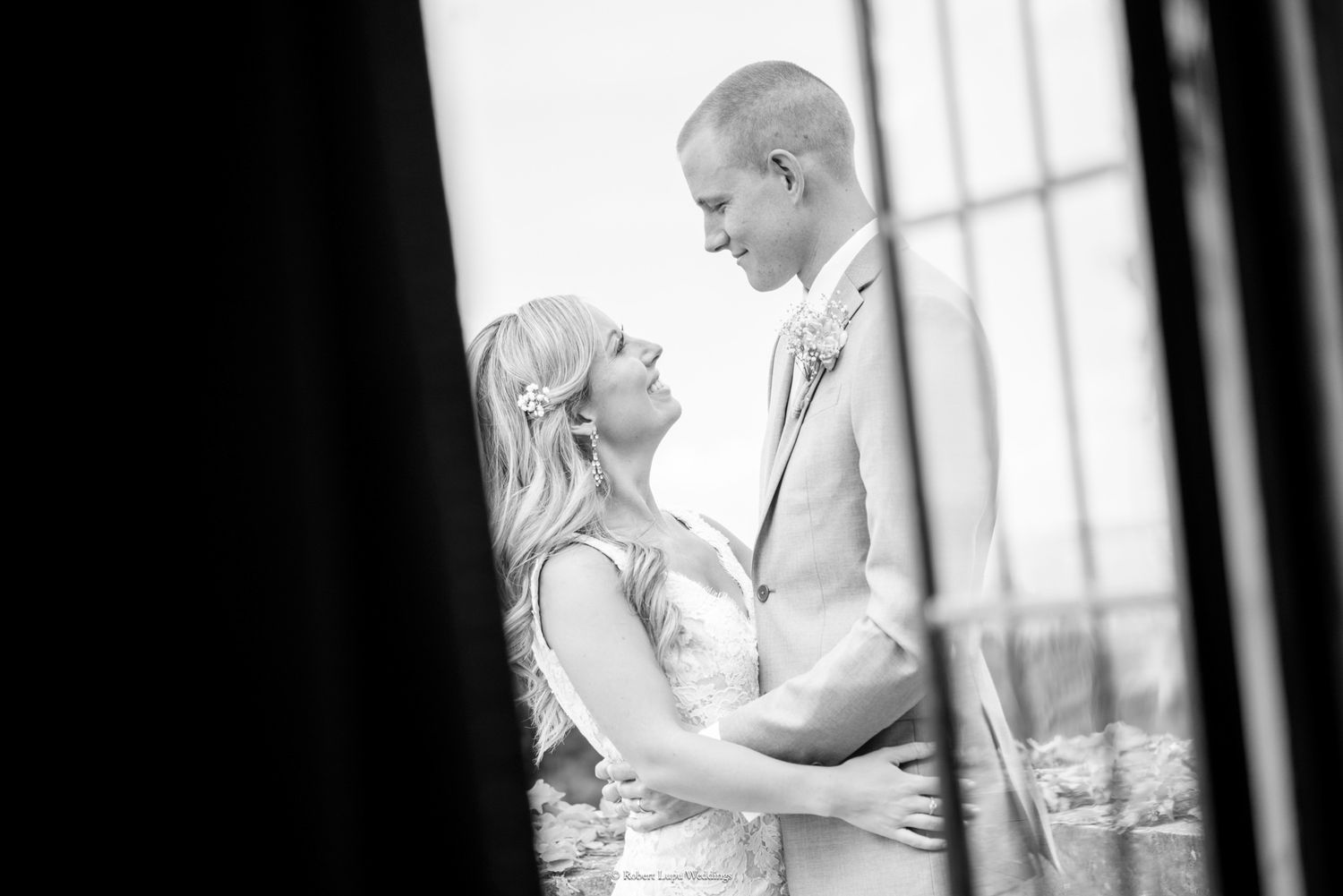 Black and white wedding portrait of bride and groom gazing at each other through a window.