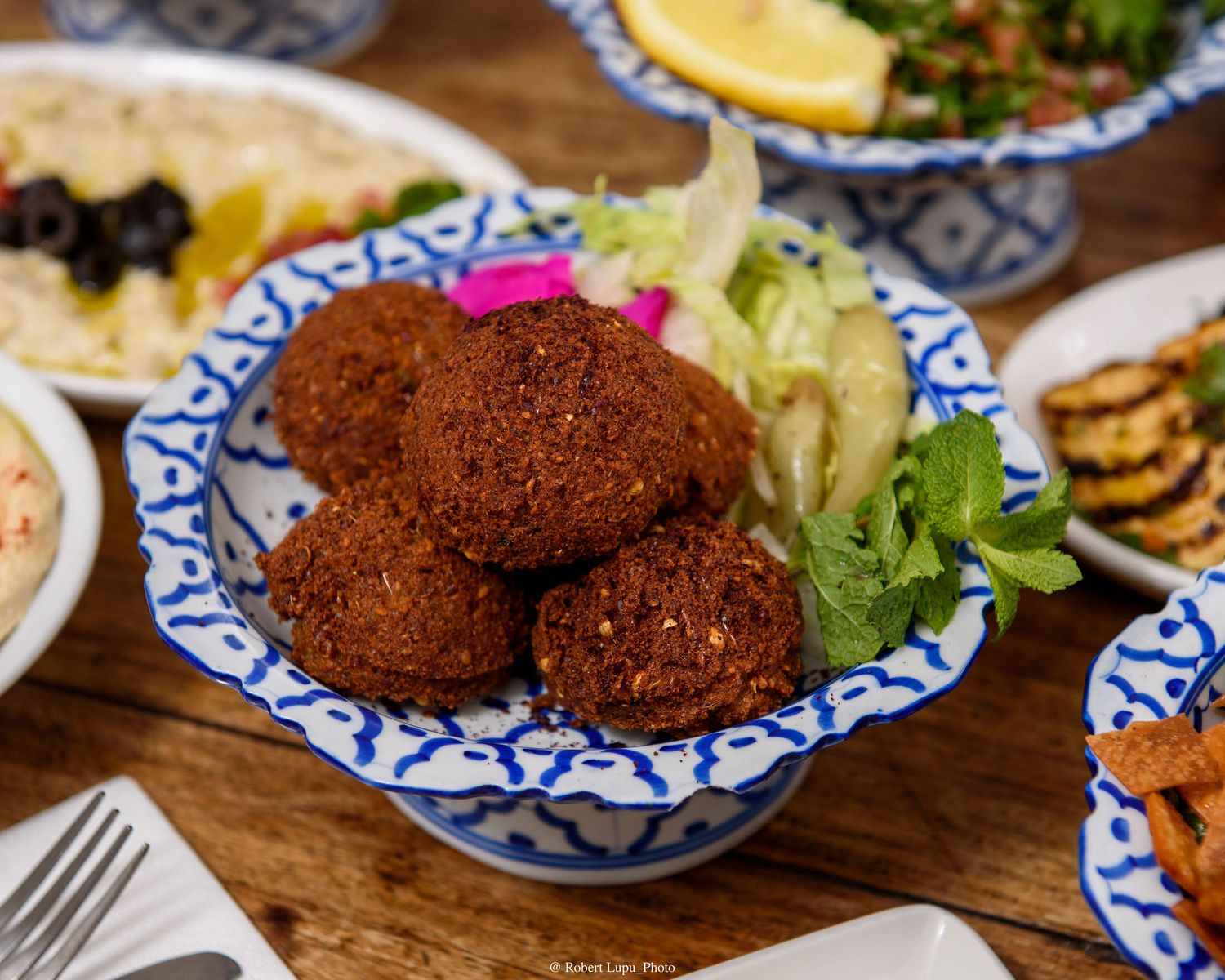 Golden falafel balls served in a blue and white bowl with fresh lettuce, mint, and pickled vegetables on a wooden table.