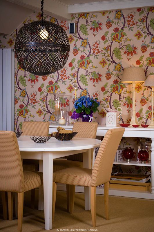 Cozy dining area with floral wallpaper, round white table, tan striped chairs, and a woven pendant light.