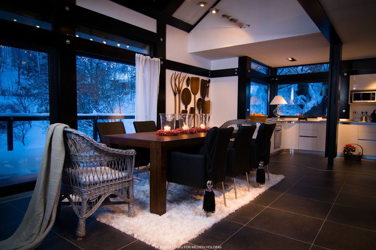 Modern dining room with dark wood table, black chairs, candles, and snowy winter view through large windows.
