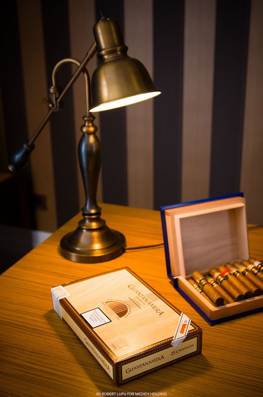 Brass desk lamp illuminating a Guantanamera cigar box and open humidor on a wooden table.