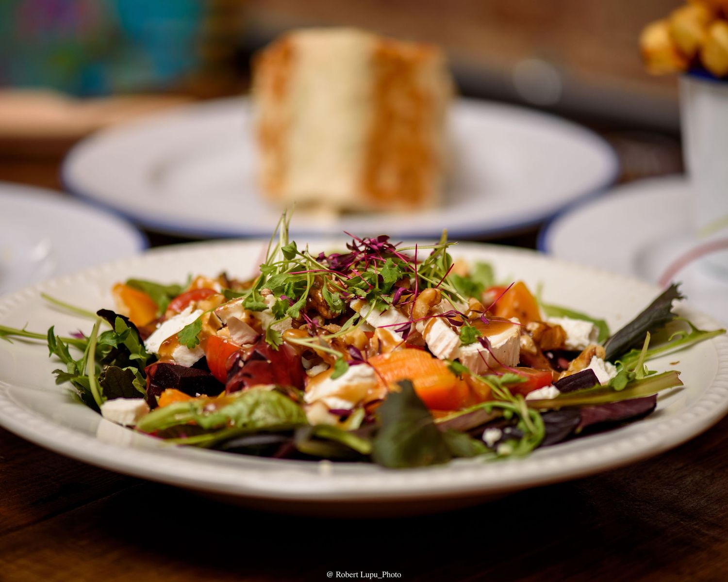 Fresh mixed greens salad with tomatoes, feta cheese, and microgreens on a white plate in a restaurant setting.