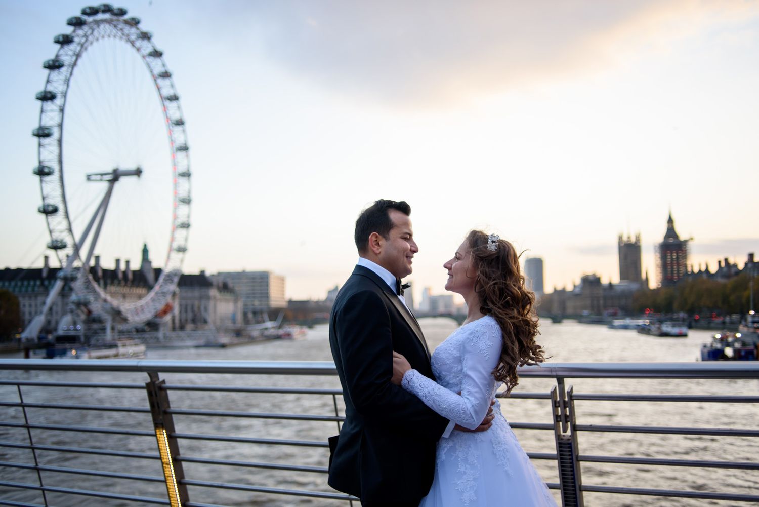 Wedding couple embracing on the Thames with the London Eye and Big Ben at sunset.