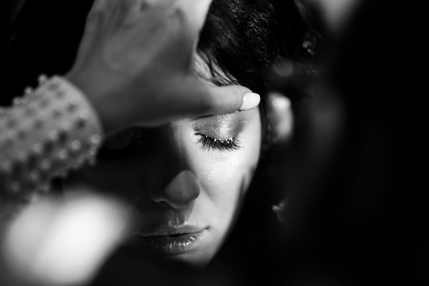 Black and white photo of a woman having makeup applied, eyes closed, showcasing elegant lashes and serene expression.
