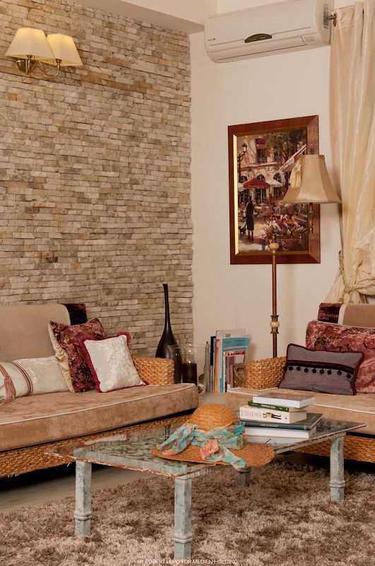 Cozy living room with exposed brick wall, tan leather sofa, colorful pillows, glass coffee table, and framed artwork.