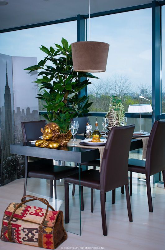 Modern dining area with large plant centerpiece, gold lion figurine, and city skyline view.