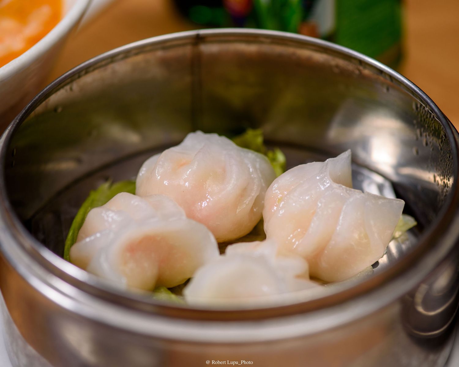 Steamed shrimp har gow dumplings served in a metal bamboo steamer basket at a dim sum restaurant.