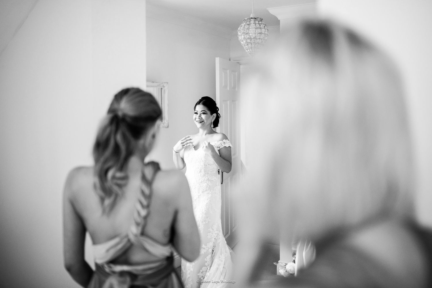 Bride in white wedding gown adjusting dress while looking in mirror, black and white photo.