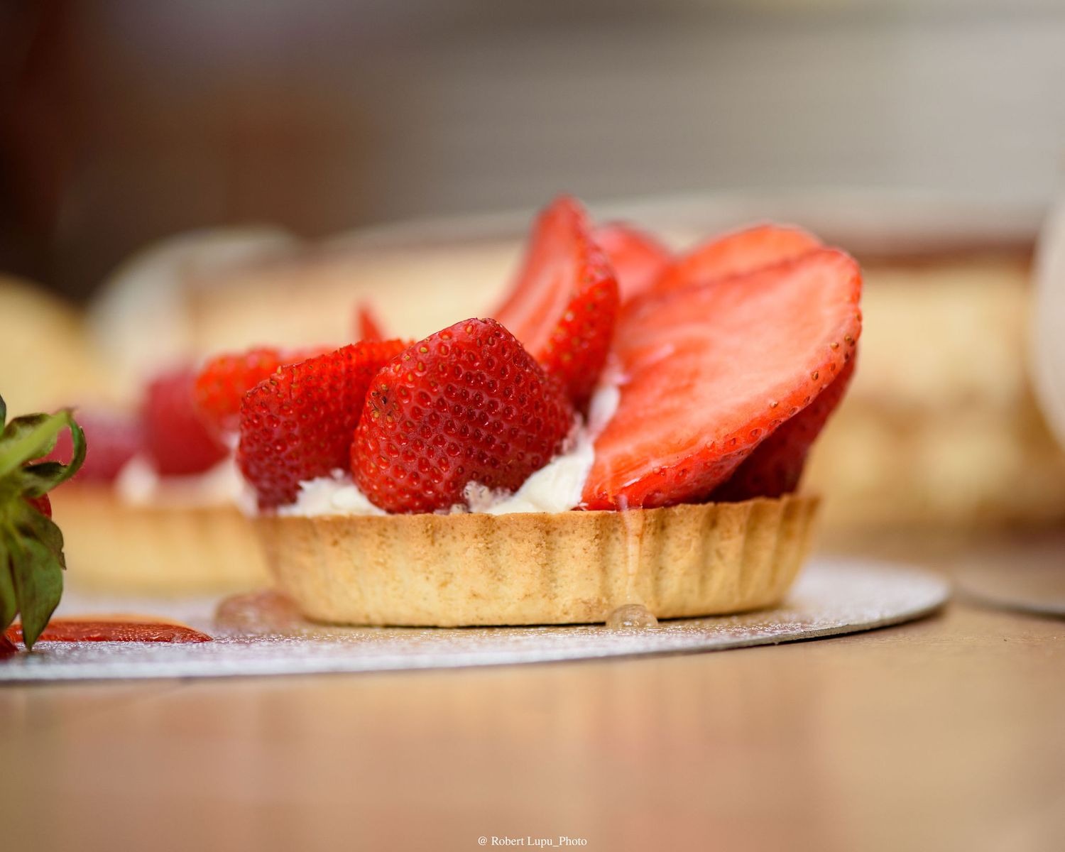 Fresh strawberry tart with whipped cream in a golden pastry shell, topped with sliced strawberries on a white plate.