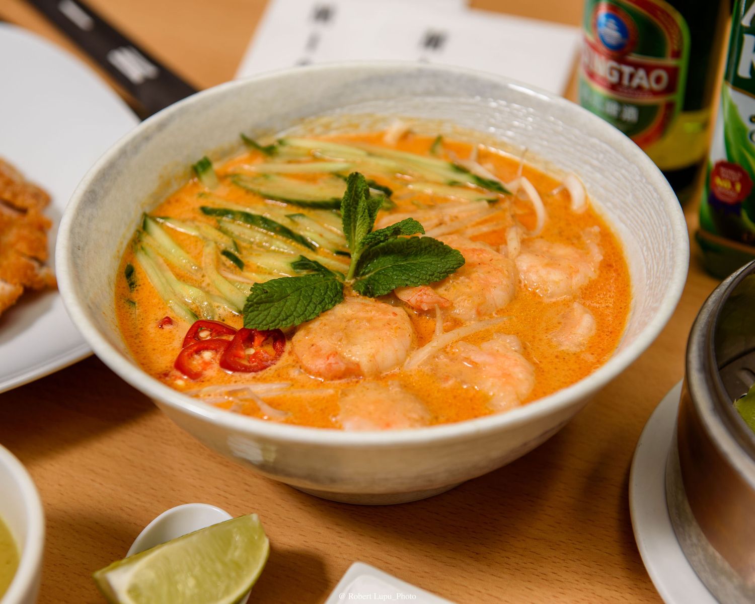 A bowl of creamy Thai shrimp noodle soup garnished with fresh herbs, chili slices, and cucumber strips.
