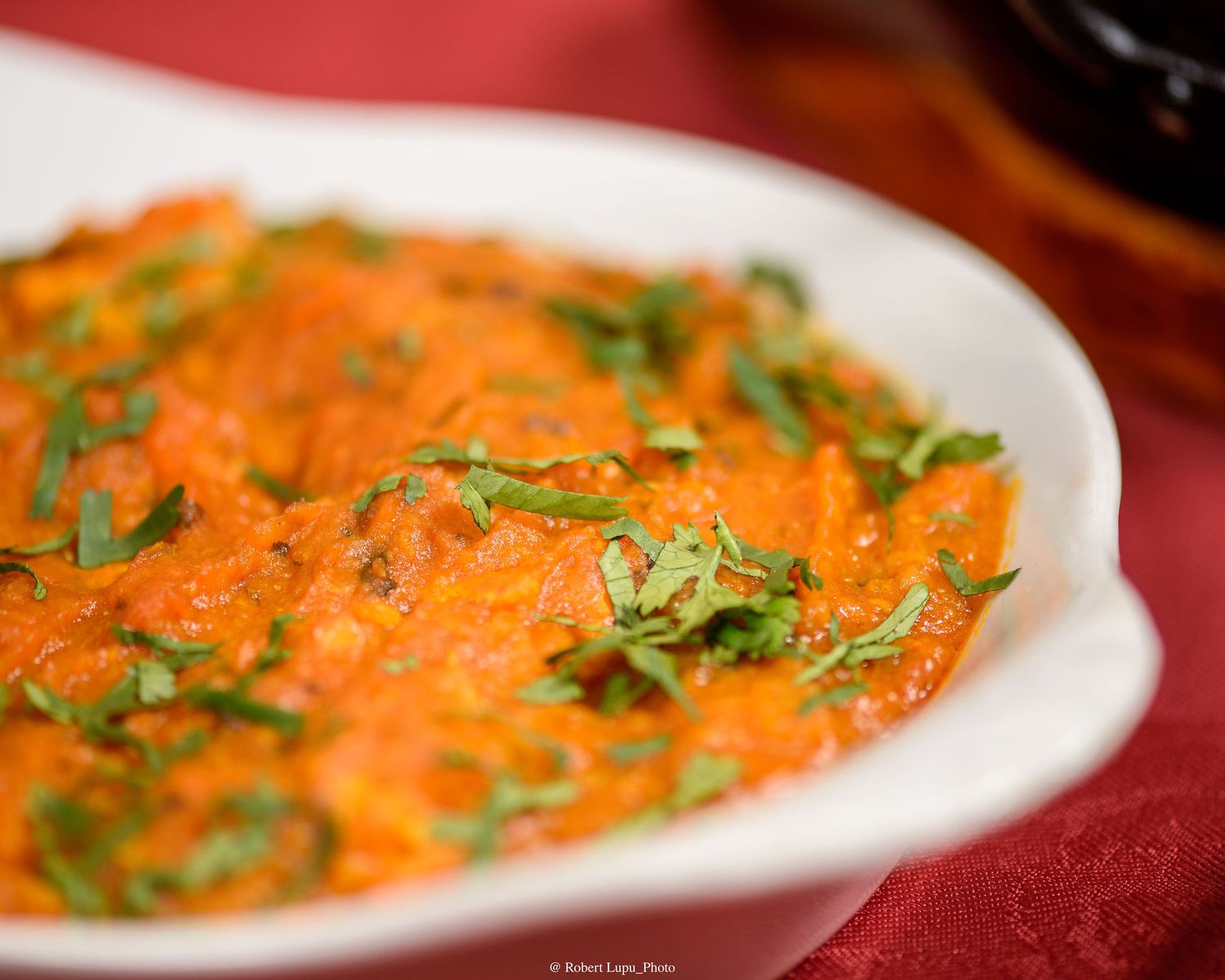 Creamy orange tomato curry garnished with fresh herbs in a white oval serving dish.