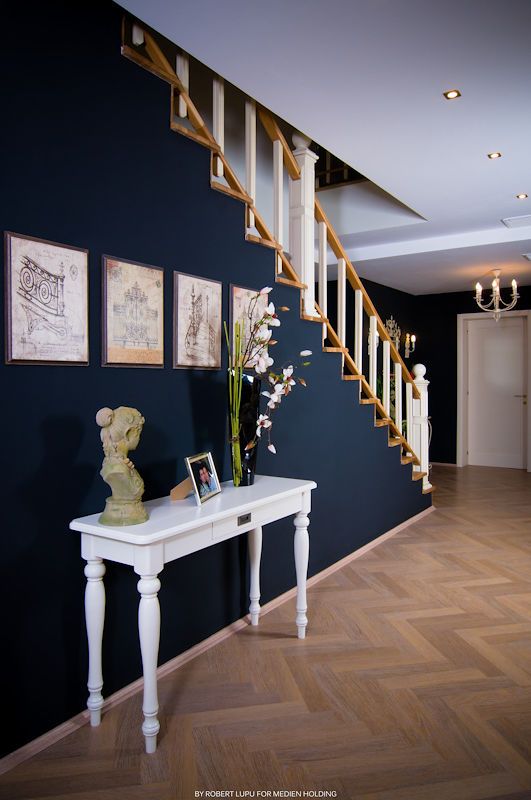Elegant hallway with navy blue walls, white console table, floral arrangement, framed artwork, and wooden staircase with white balusters.