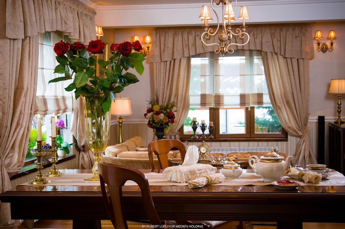 Elegant dining table set with fine china, red roses, and chandelier lighting in a classic formal dining room.