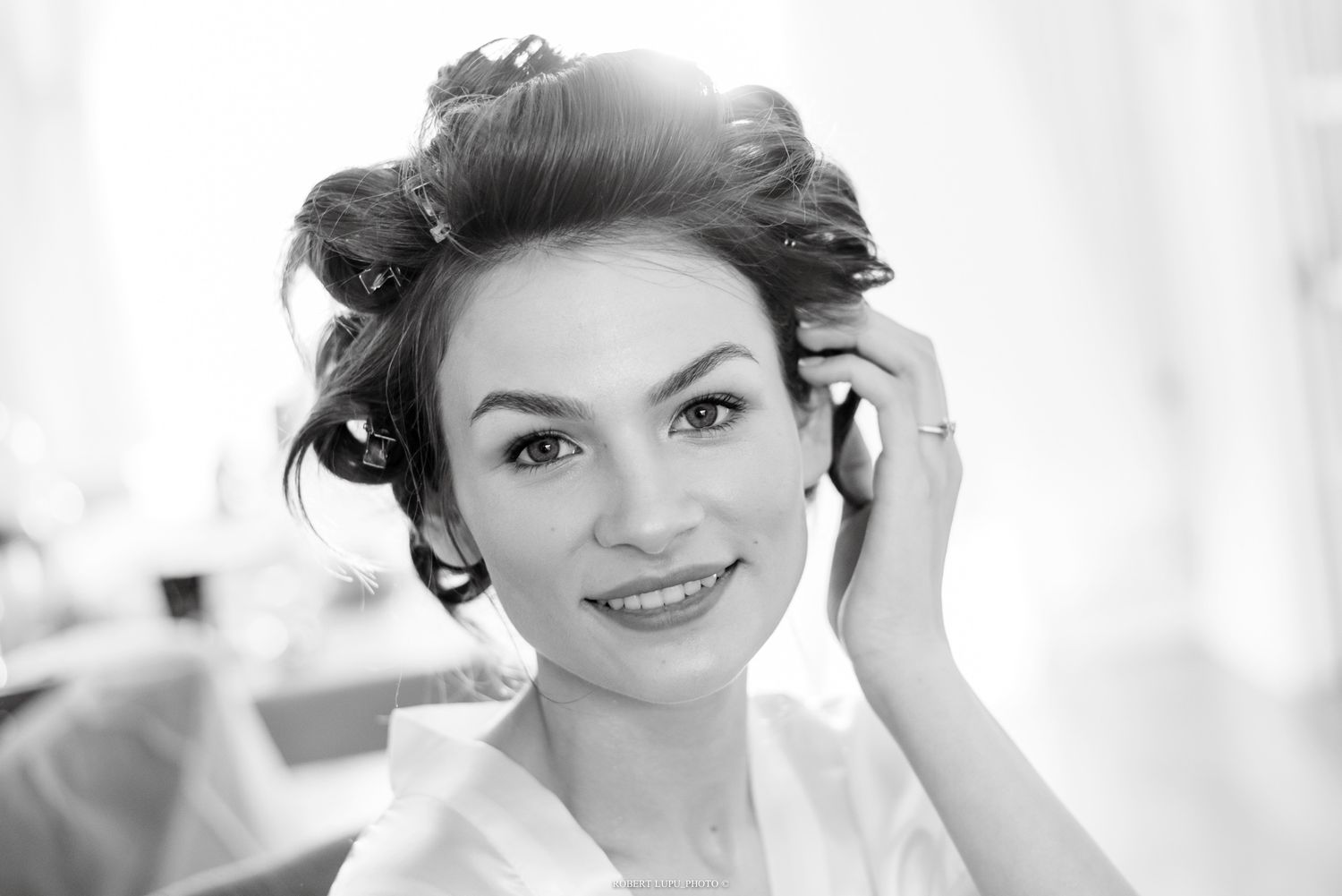 Beautiful bride smiles softly with elegant updo hairstyle while getting ready on her wedding day in black and white.