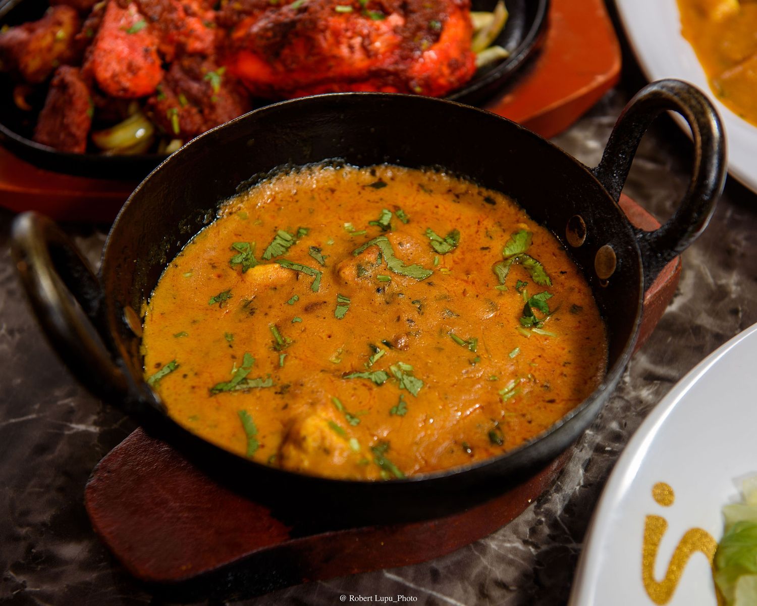 A rich and creamy Indian curry garnished with fresh herbs, served in a traditional black iron kadai pan.
