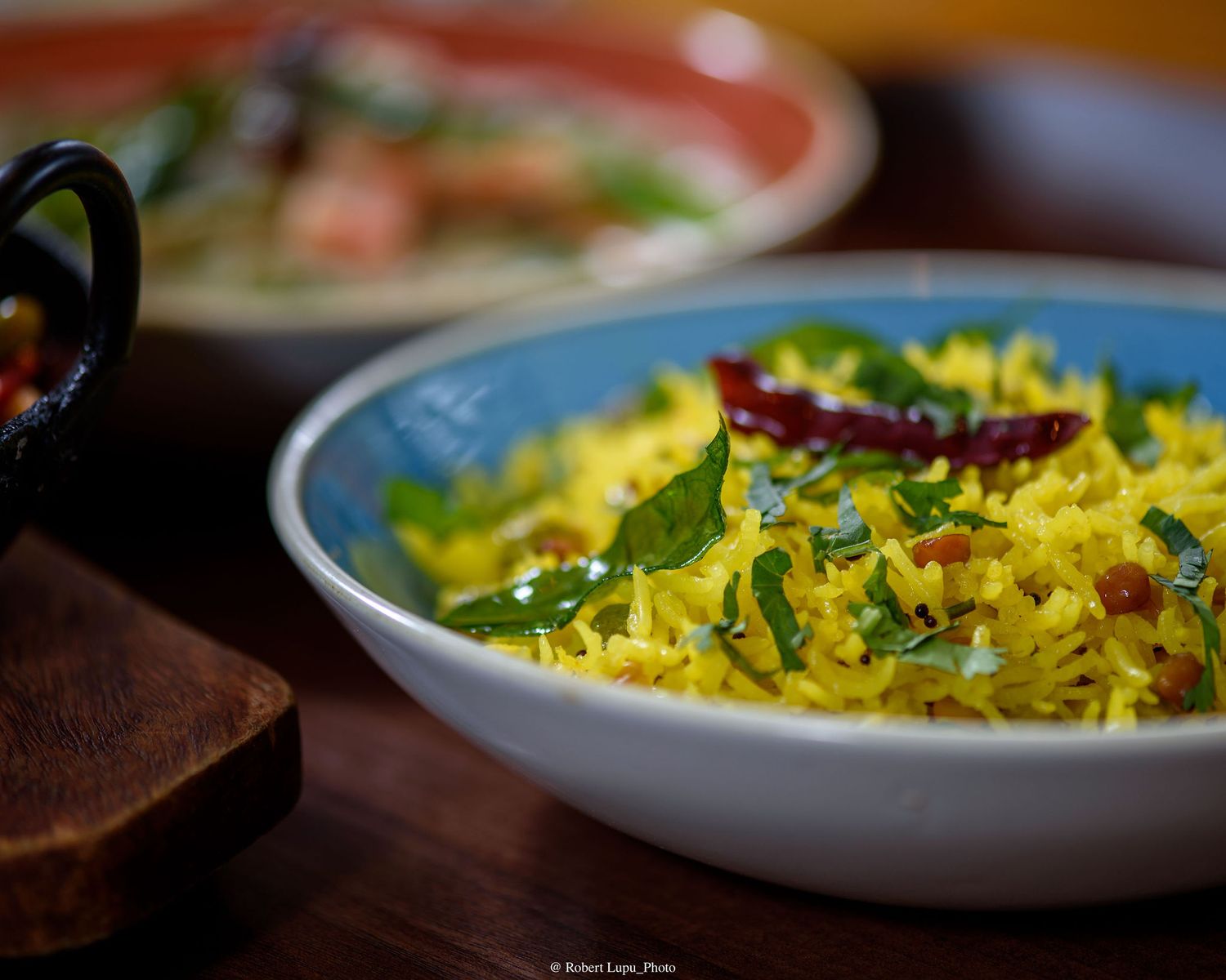 A vibrant bowl of yellow turmeric rice garnished with curry leaves and red chilies, served in a blue ceramic bowl.