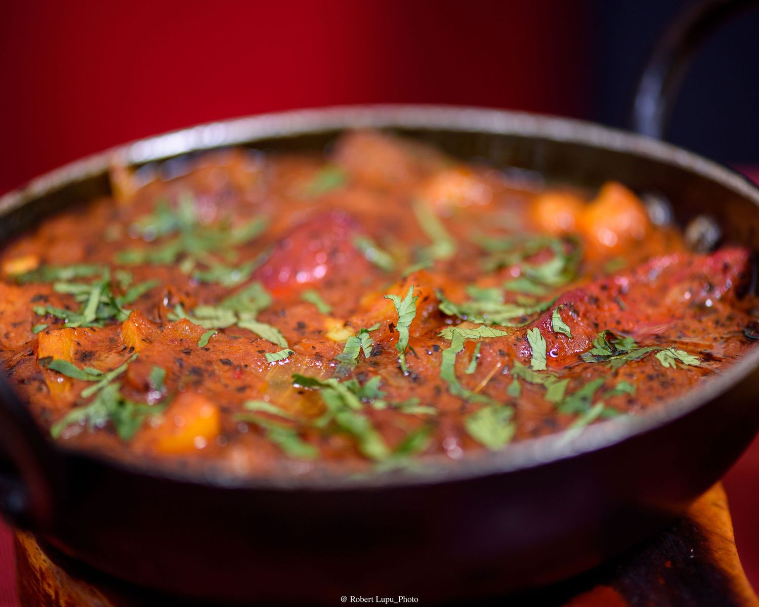 A rich tomato-based curry with vegetables and fresh basil in a traditional black iron karahi pan.