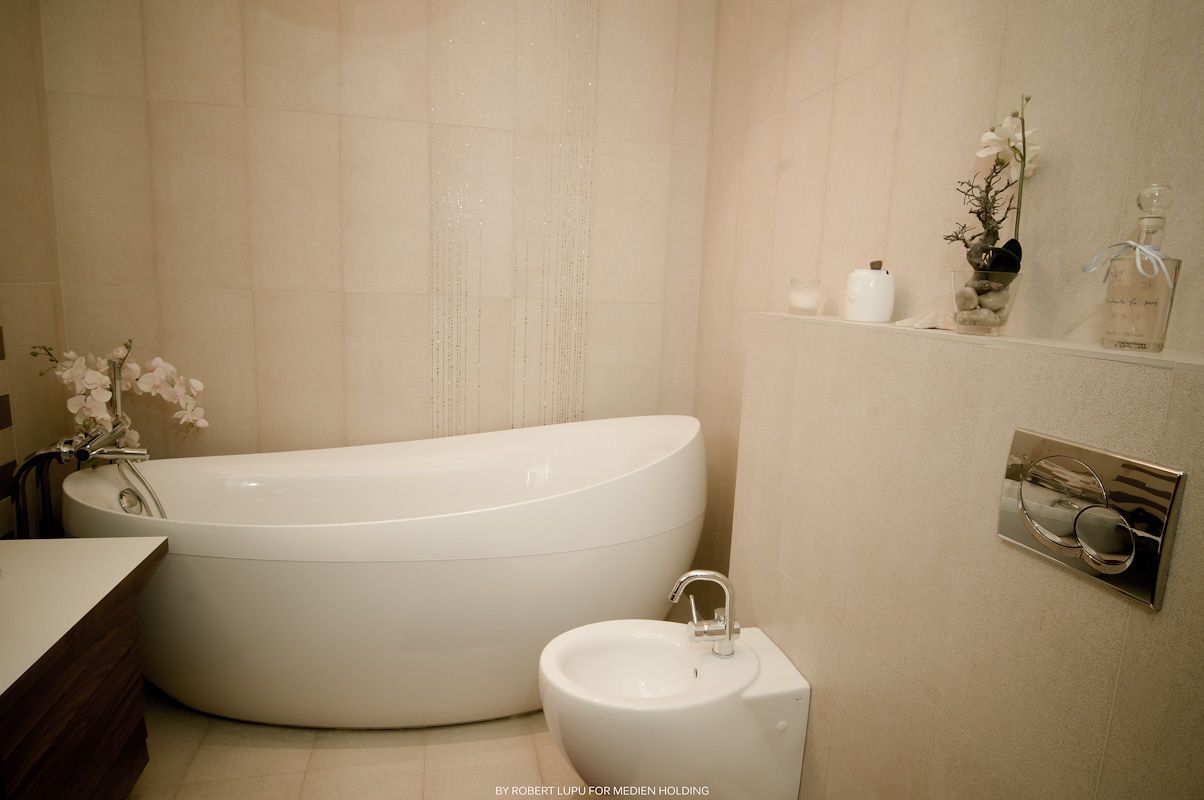 Modern beige bathroom with freestanding oval white bathtub, bidet, built-in shelf, and elegant orchid decor.