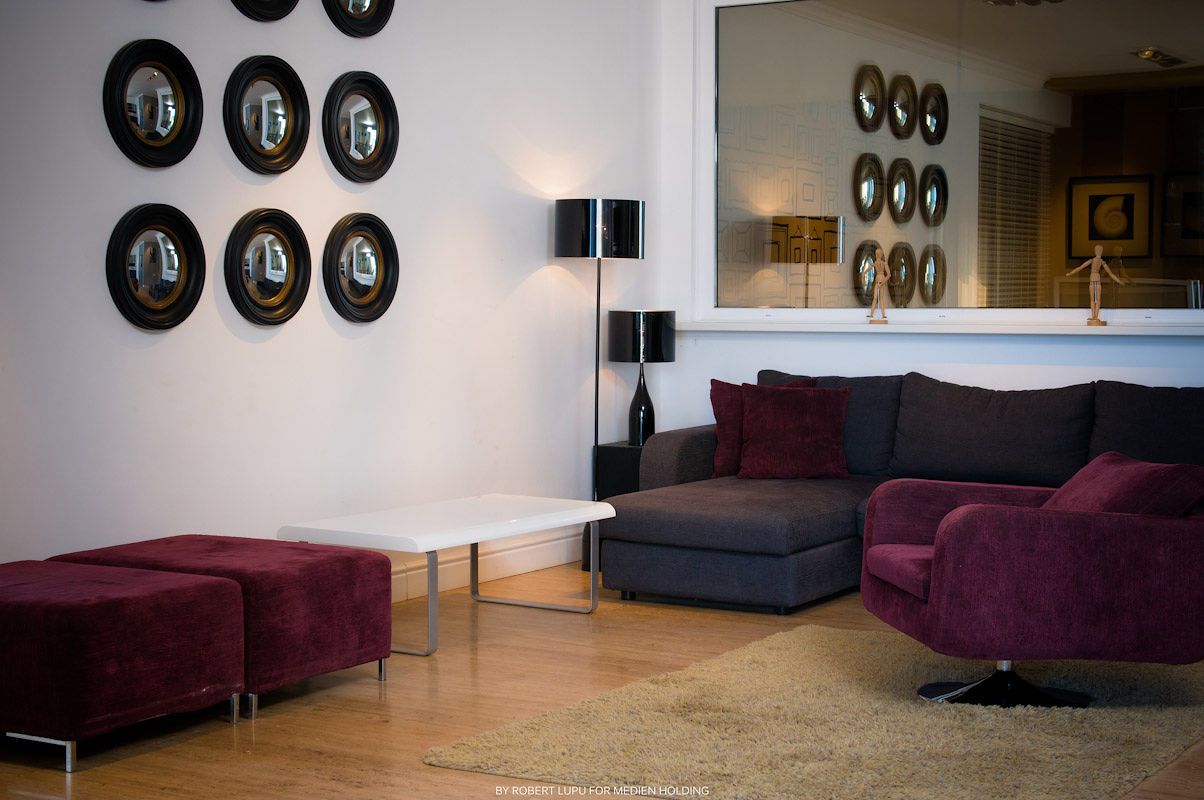 Modern living room with purple velvet sofa, chaise lounge, round black mirrors on white wall, and floor lamp.