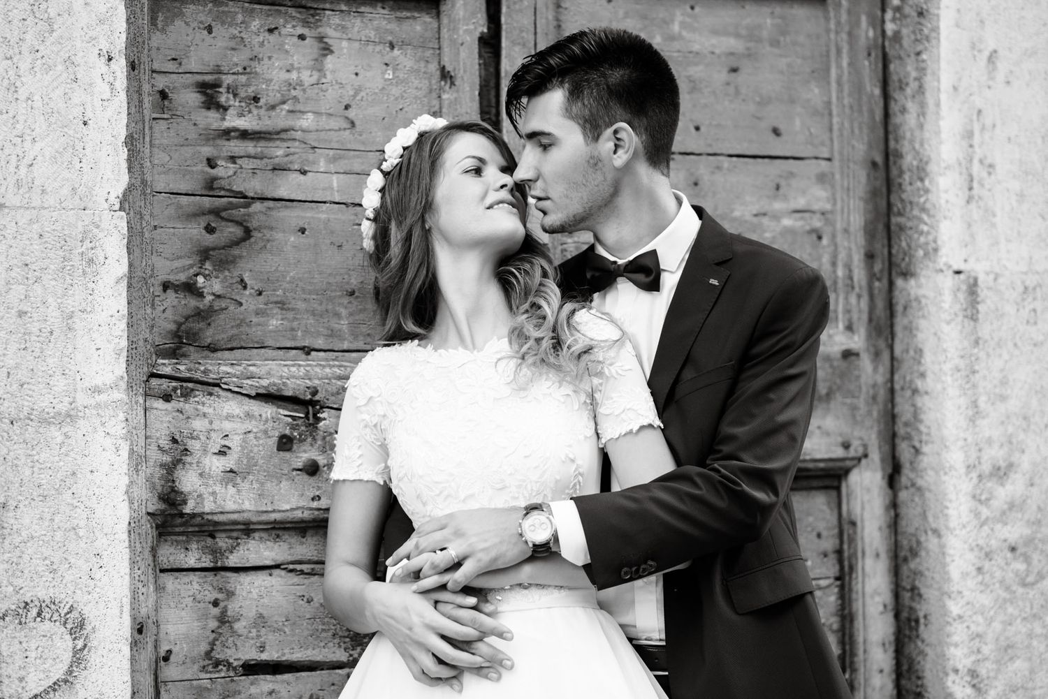 Black and white wedding photo of a couple embracing tenderly in front of a rustic wooden door.