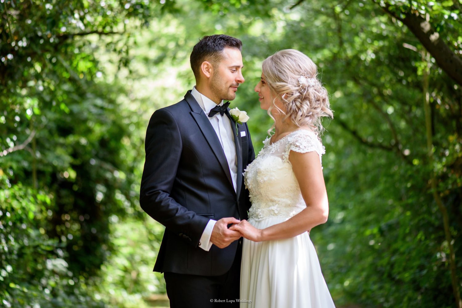 Bride and groom holding hands in a lush green garden tunnel, sharing a romantic moment on their wedding day.