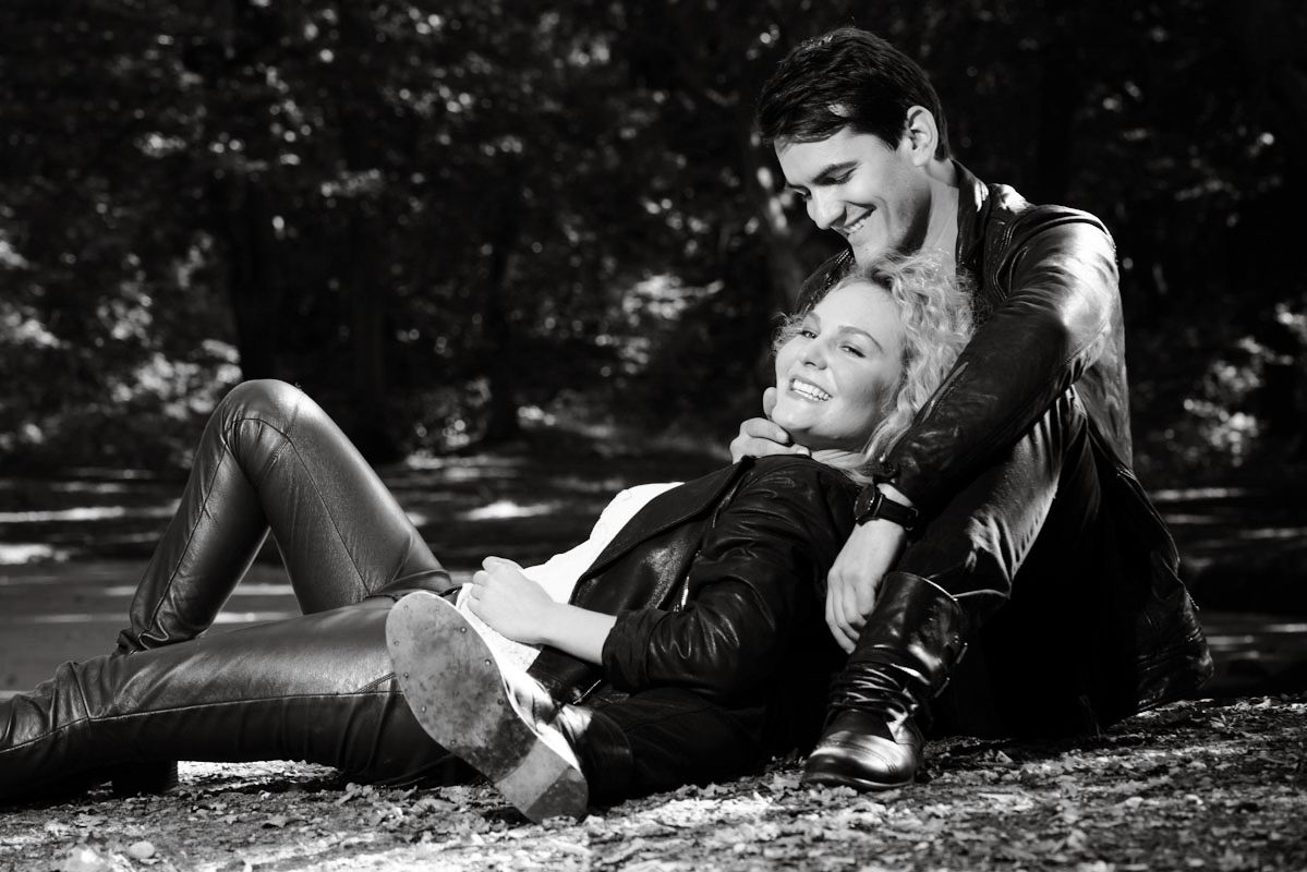 Black and white photo of a smiling couple relaxing together outdoors in a park, wearing leather jackets.