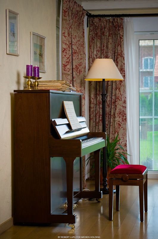 Elegant upright piano with sheet music, purple candles, floor lamp, and red curtains in a cozy living room.