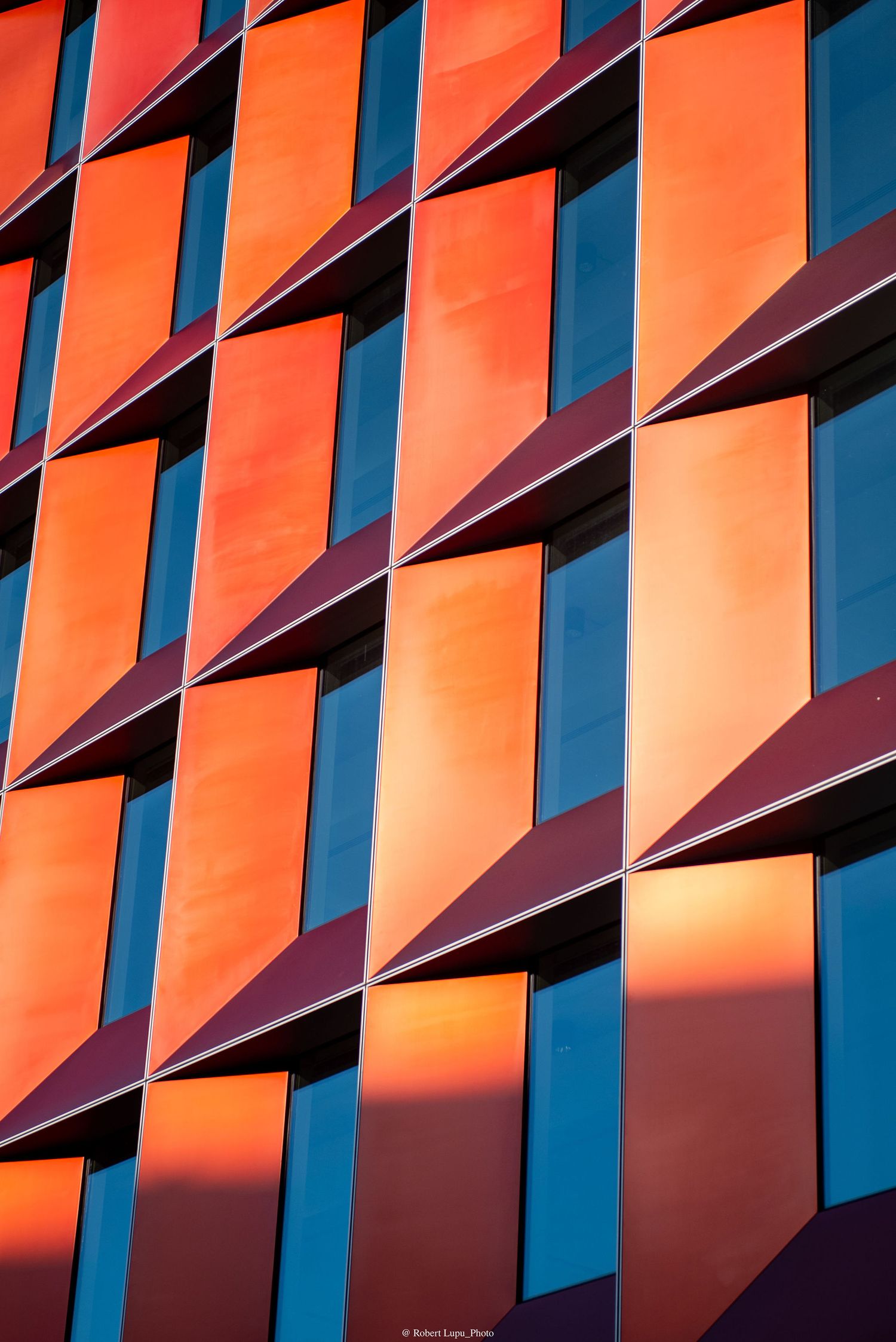 Modern building facade with vibrant orange and red geometric panels reflecting sunset light in an abstract pattern.