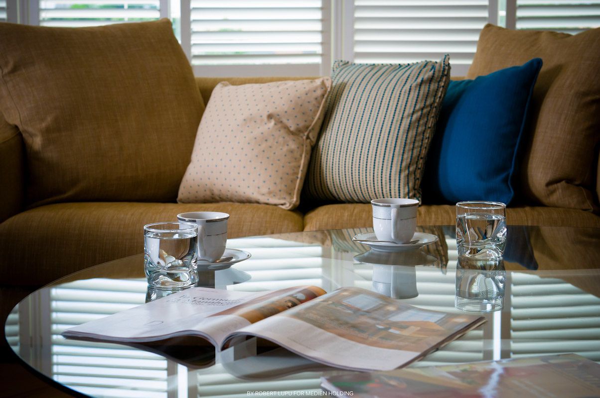 Cozy living room with tan sofa, decorative pillows, glass coffee table with water glasses and open magazine.
