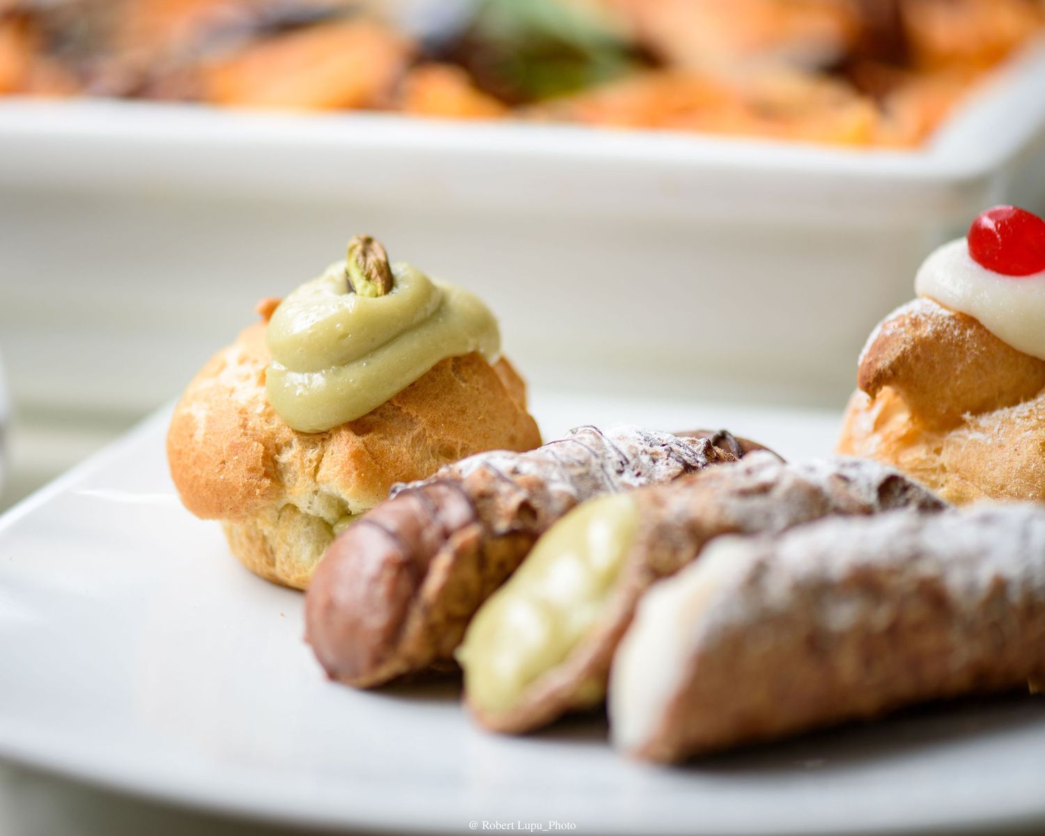 Assorted Italian pastries including cannoli and cream puffs with pistachio frosting served on a white plate.