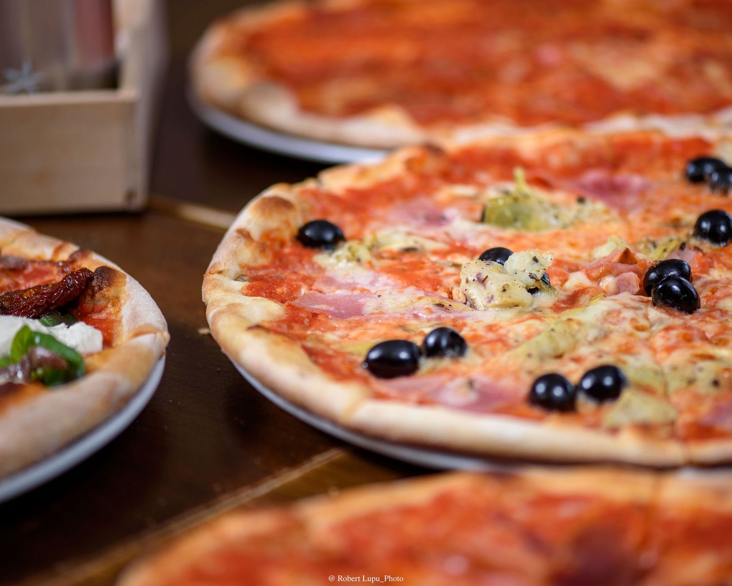 Freshly baked pizza topped with black olives, ham, cheese, and tomato sauce served on a white plate.