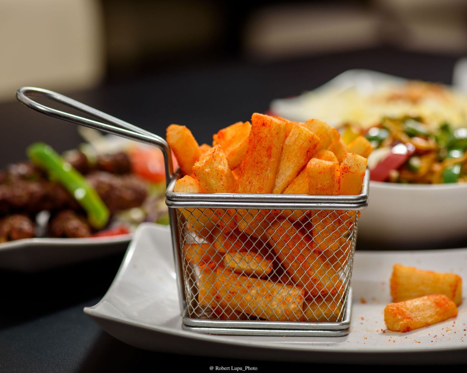 Golden crispy sweet potato fries served in a mini metal basket on a white plate at a restaurant.