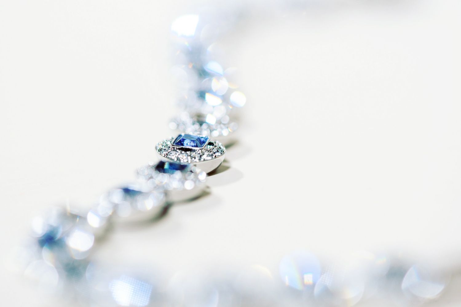 Close-up of a diamond and sapphire pendant necklace with sparkling blue gems on a white background.