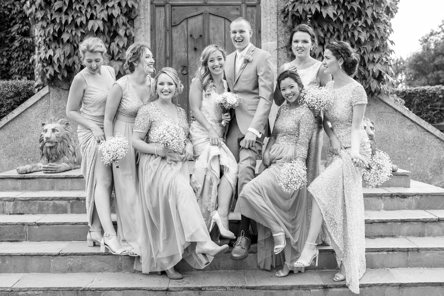 Black and white wedding photo of bride, groom, and bridesmaids posing on stone steps with bouquets.