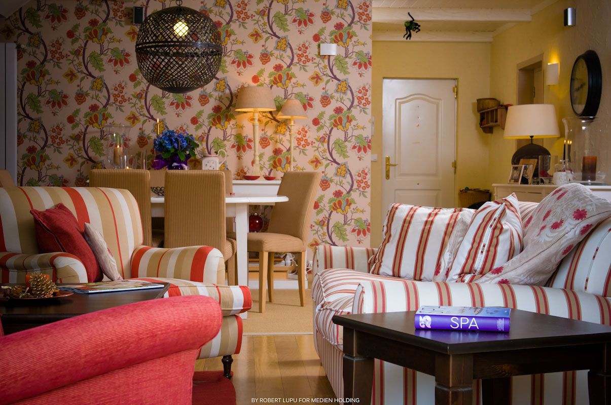 Cozy living room with striped sofas, floral wallpaper, dark coffee table, and warm lighting in a cottage-style interior.