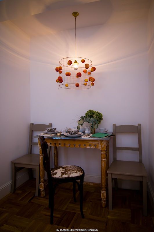 Elegant dining nook with gold chandelier adorned with orange spheres above a vintage wooden table set for two.