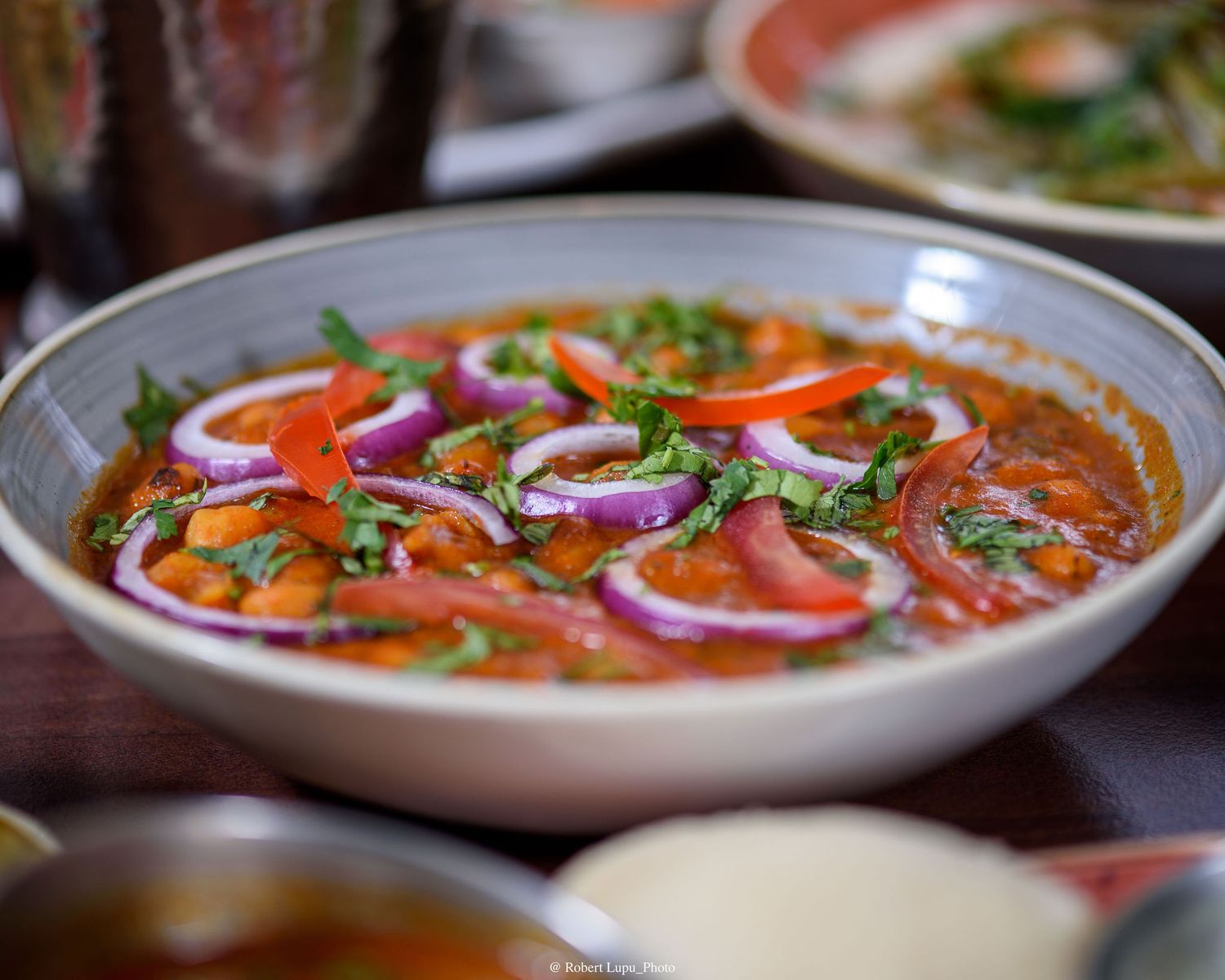 A vibrant bowl of Indian chickpea curry topped with red onions, bell peppers, and fresh cilantro.
