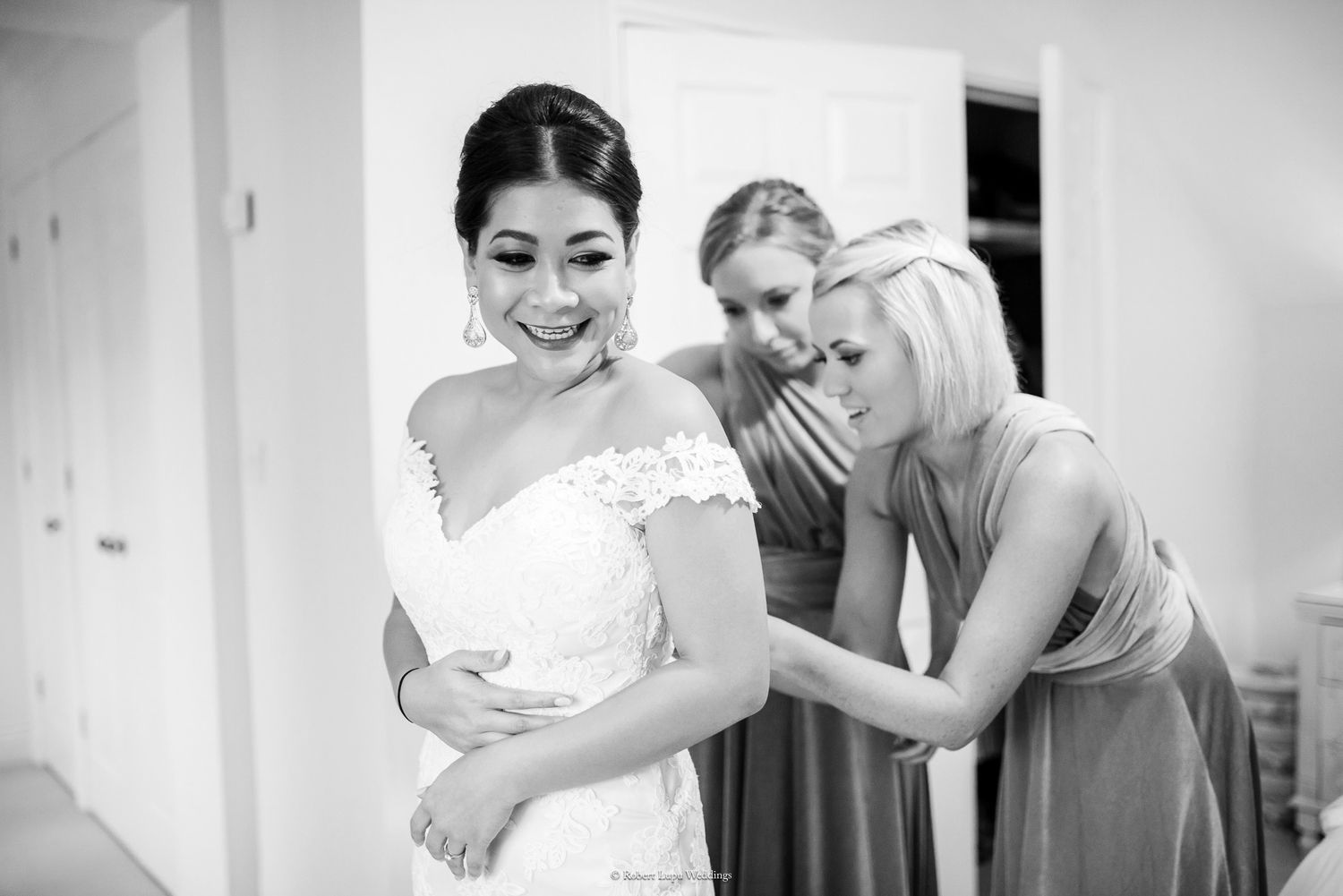 Bridesmaids help bride with her lace off-shoulder wedding dress in black and white getting ready photo.