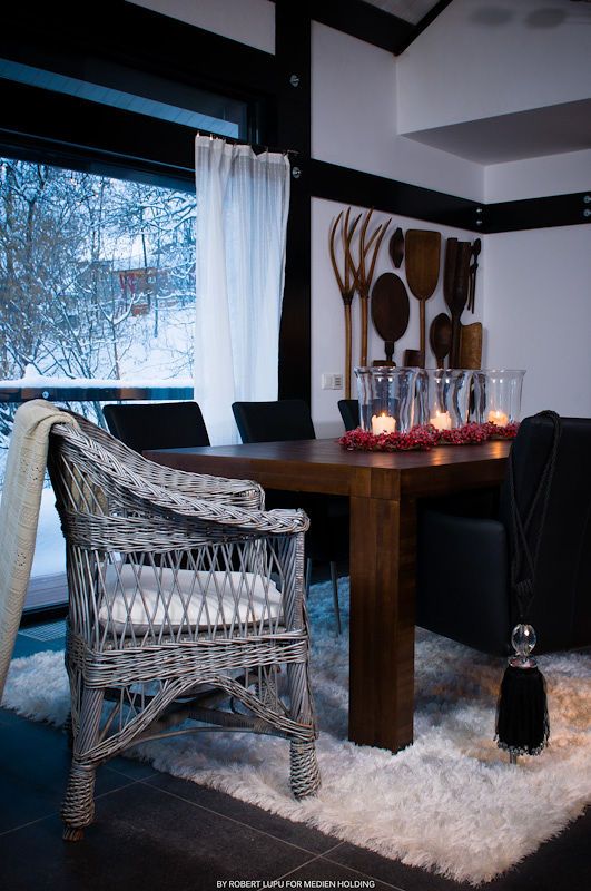 Elegant dining area with wicker chair, wooden table, candles, and decorative wall art in a winter chalet setting.