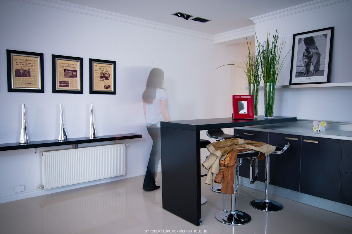 Modern kitchen bar area with black countertop, bar stools, framed wall art, and a woman standing near the counter.