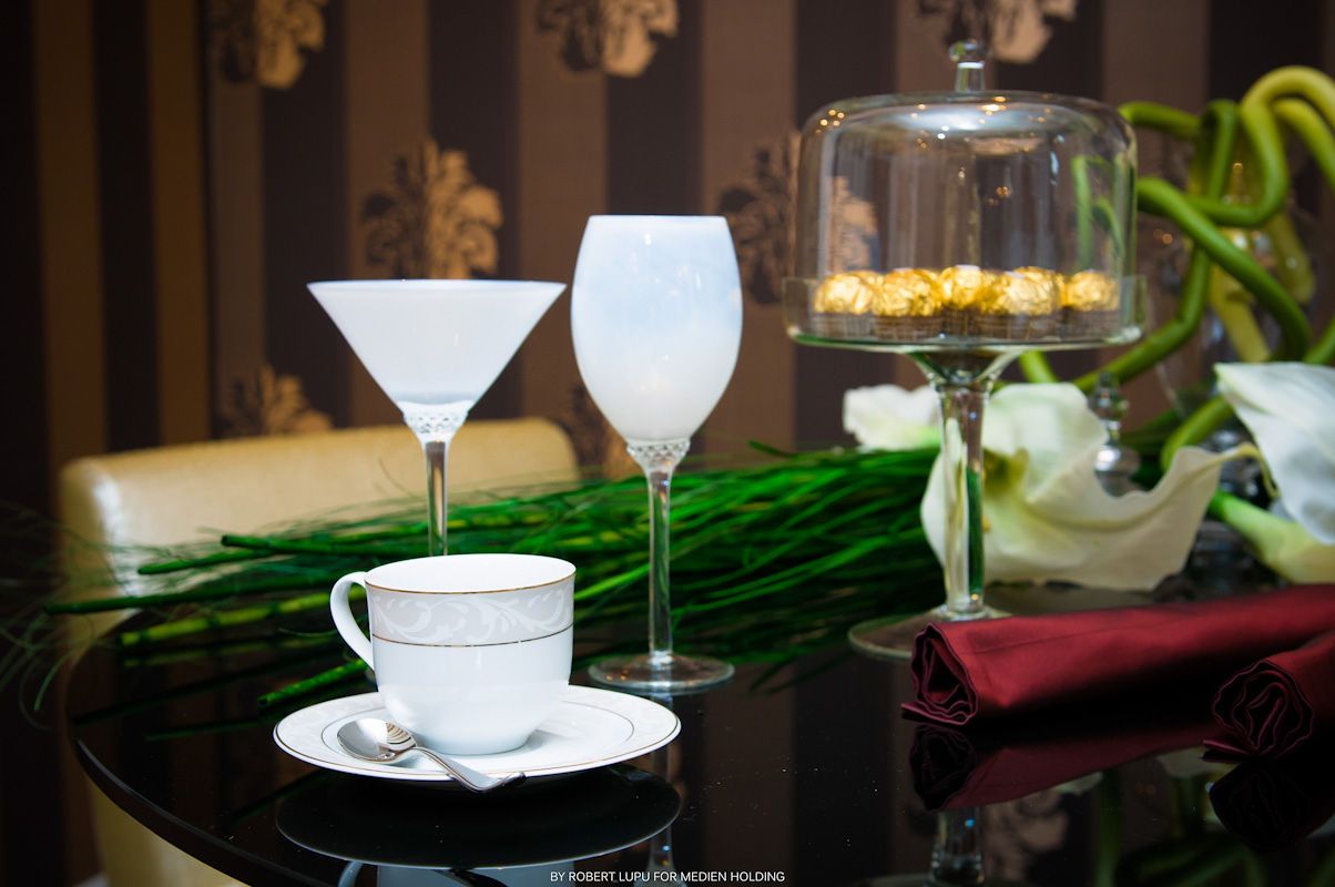 Elegant table setting with martini glass, wine glass, coffee cup, and dessert stand on a reflective surface.