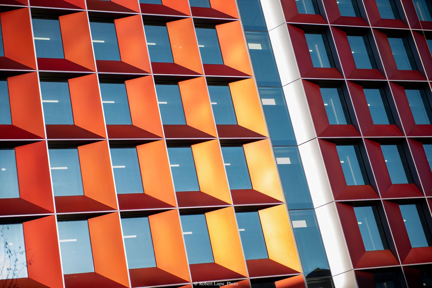Colorful modern building facade with geometric orange and red panels framing large glass windows in an abstract pattern.