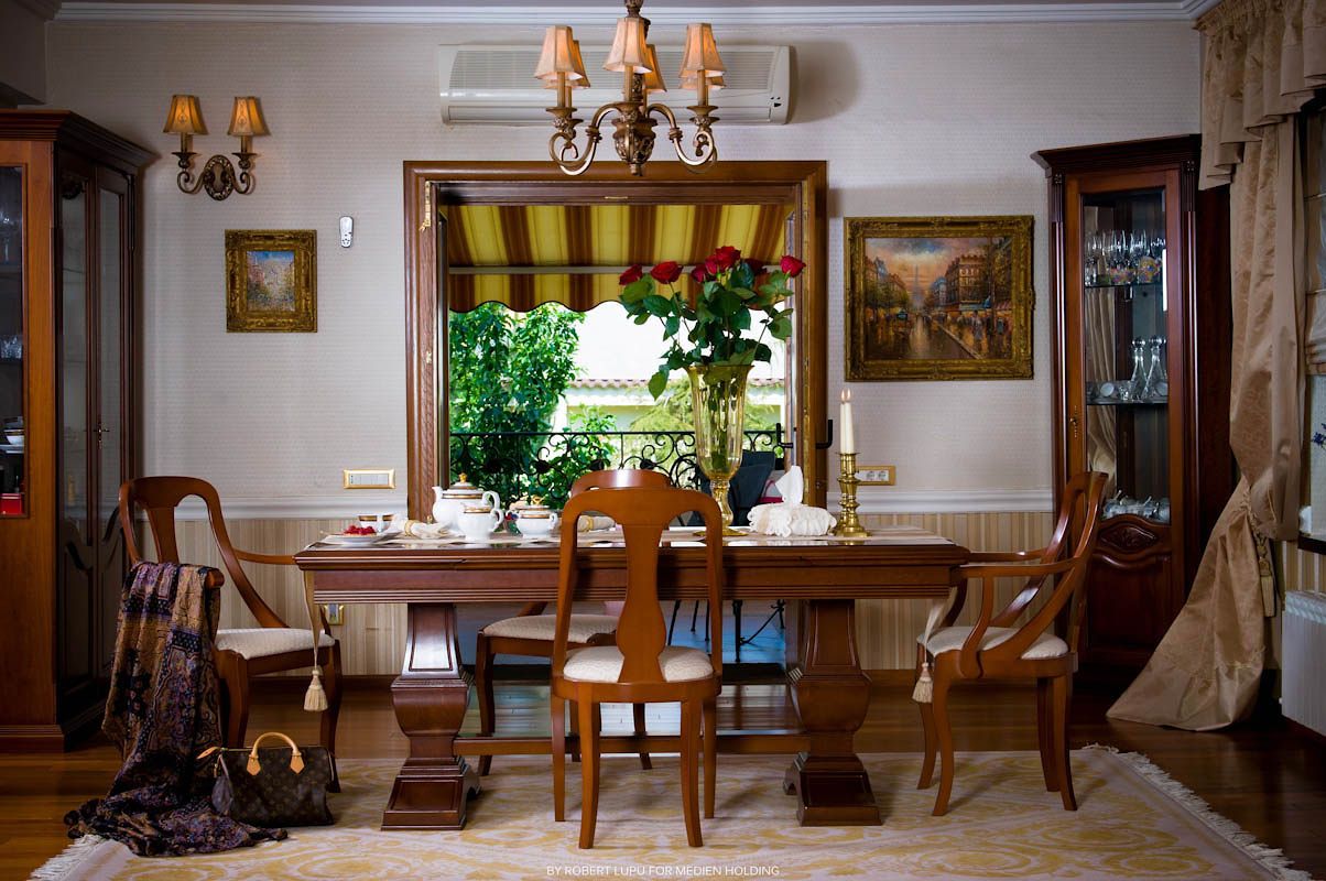 Elegant dining room with wooden table, chairs, chandelier, framed art, and a window with striped awning overlooking greenery.