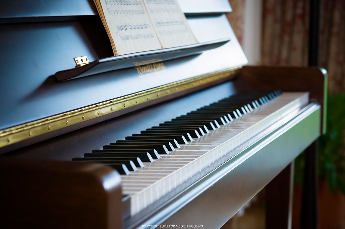 Close-up of an upright piano keyboard with sheet music on the stand, showcasing elegant wooden finish.