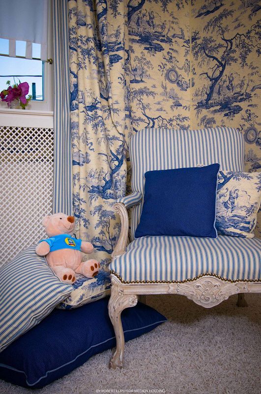 Blue and white striped French armchair with toile wallpaper, navy pillow, and pink teddy bear in elegant nursery room.