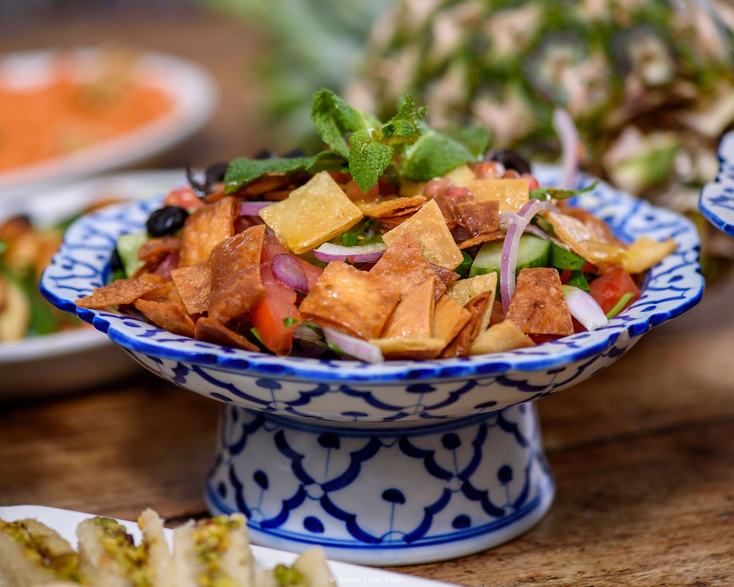 Fattoush salad in ornate blue and white ceramic bowl with crispy pita chips, tomatoes, cucumbers, and fresh herbs.